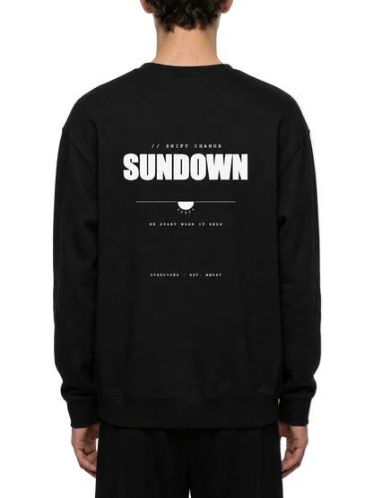 Back view of a model wearing the Steelvora SUNDOWN oversized black crewneck sweatshirt featuring a bold white SUNDOWN graphic print.